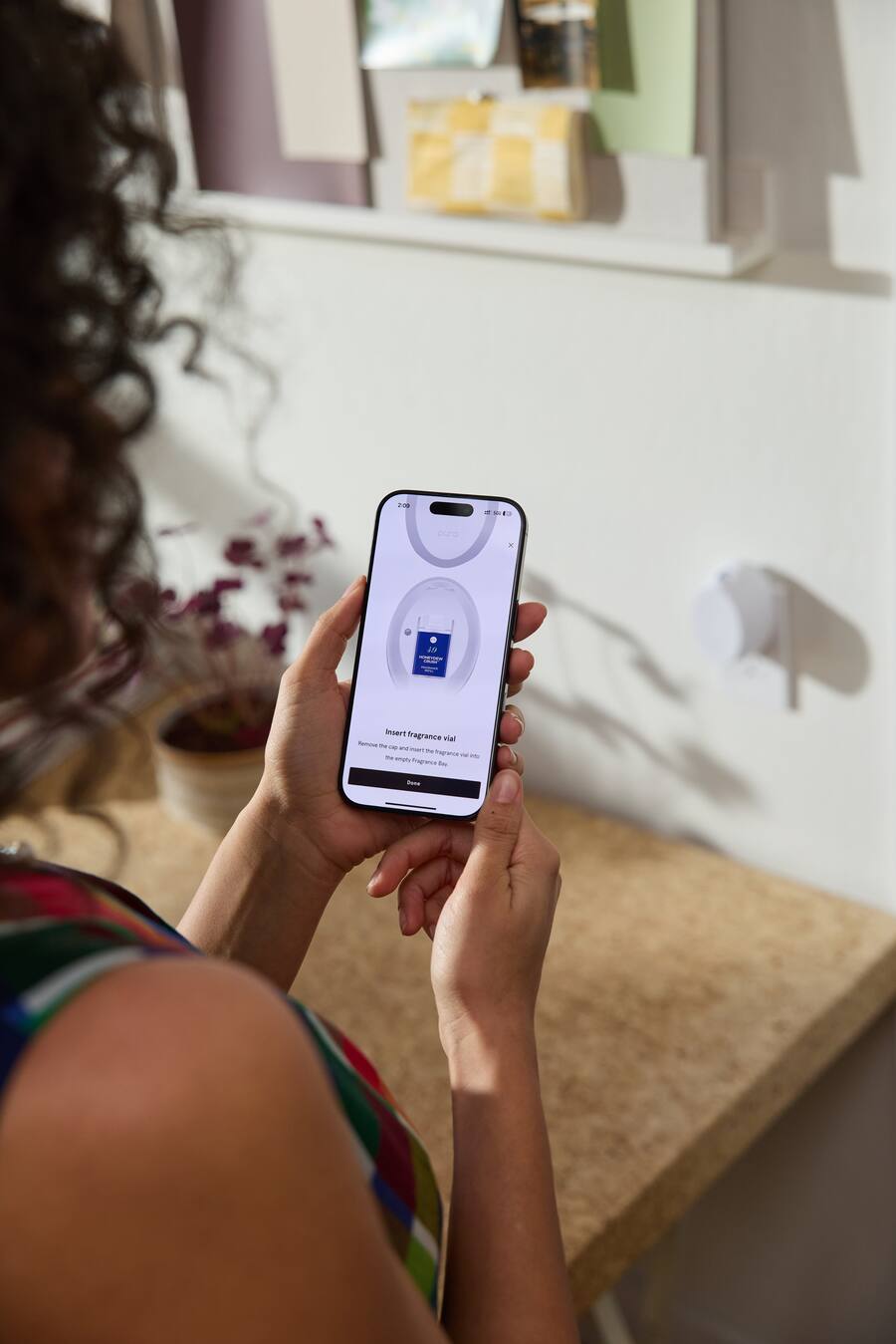 Person holding a smartphone with an app on the screen in a home setting