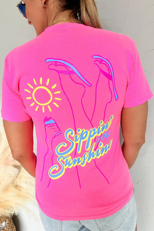 Person wearing a pink t-shirt with a sun and beach-themed design on the back.