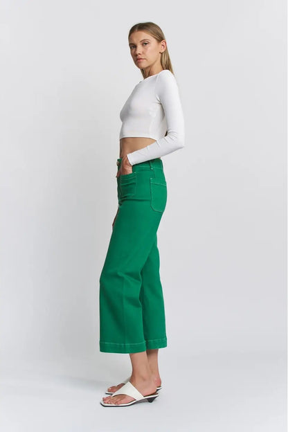 Woman wearing a white long-sleeve top and green pants on a white background