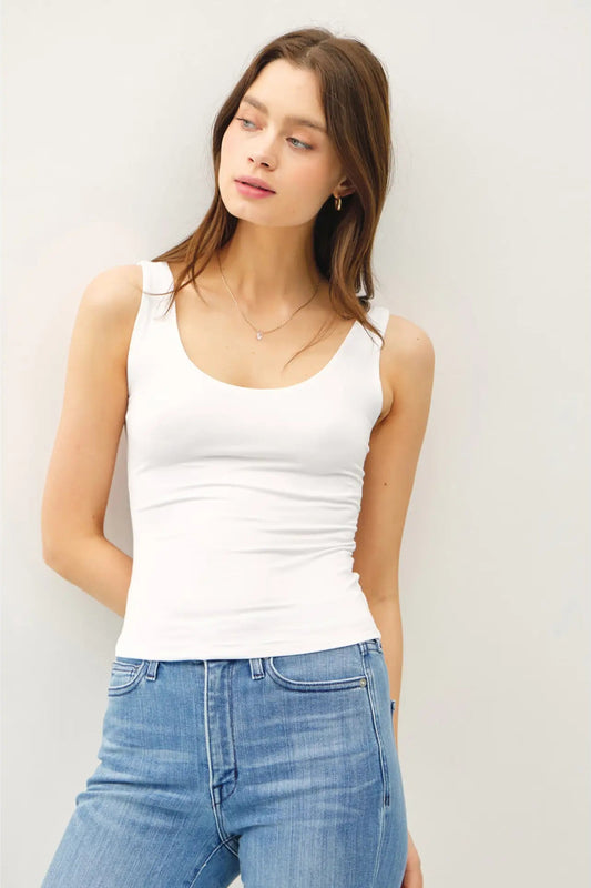 Woman wearing a white tank top and blue jeans against a light background