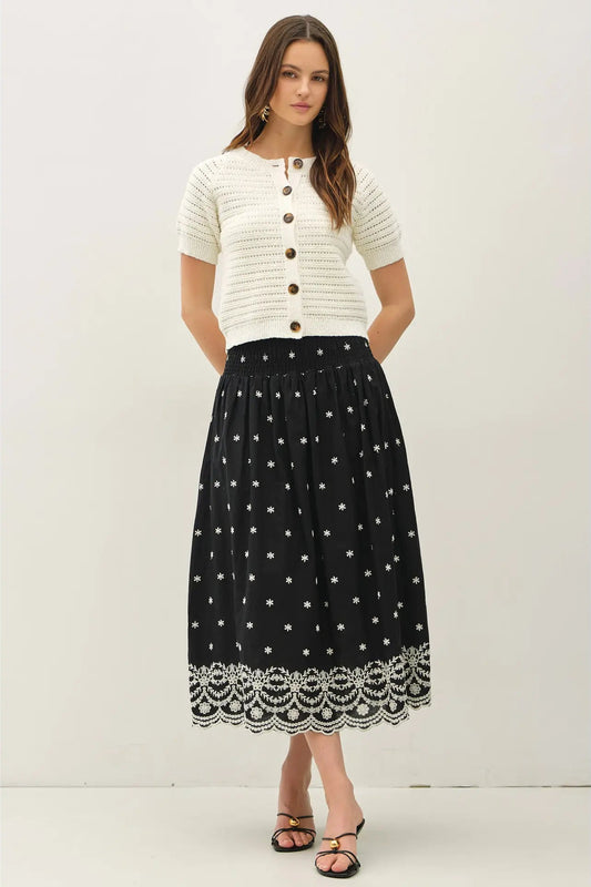 Woman wearing a white top and black skirt with white patterns on a white background