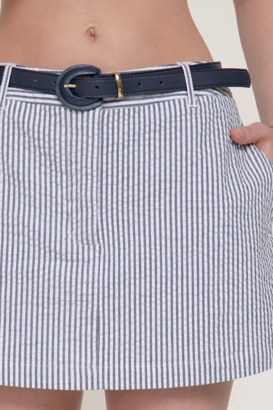 Close-up of a person wearing a navy blue and white vertically striped skirt with a navy belt featuring a gold buckle.