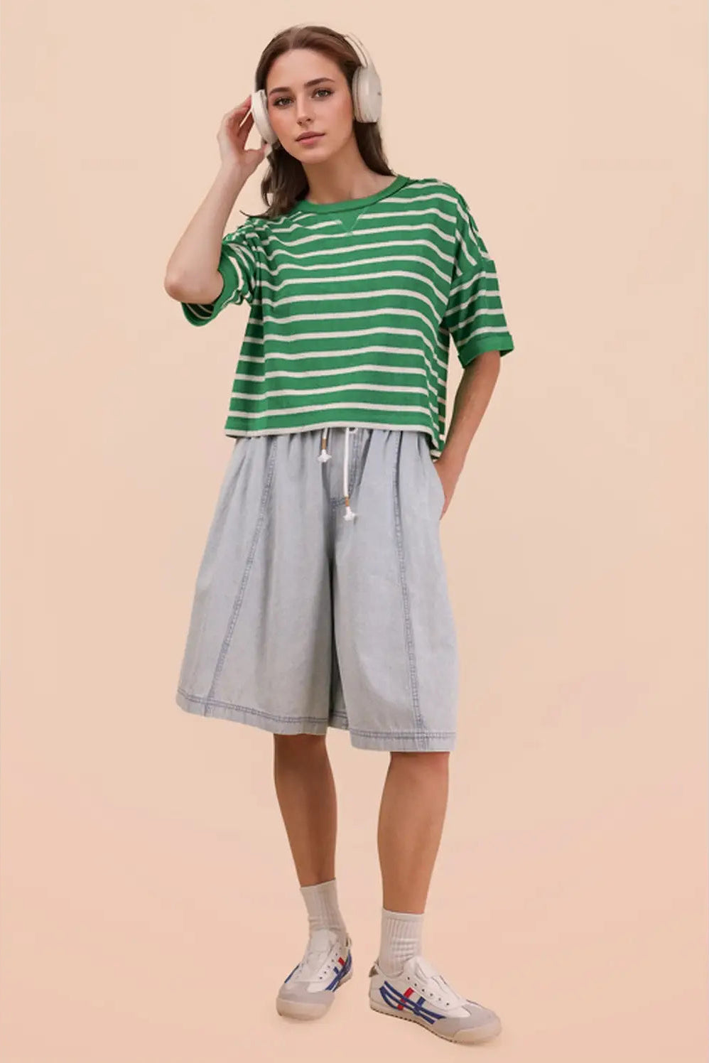 Woman wearing a green and white striped shirt with light blue shorts on a beige background