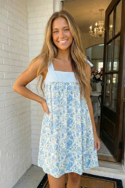 Woman wearing a blue floral dress standing in a home setting.
