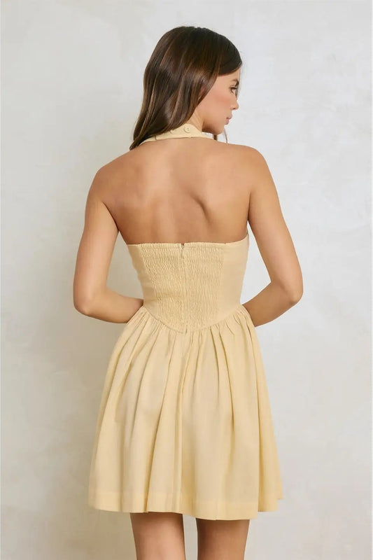 Woman wearing a beige halter neck dress against a plain background