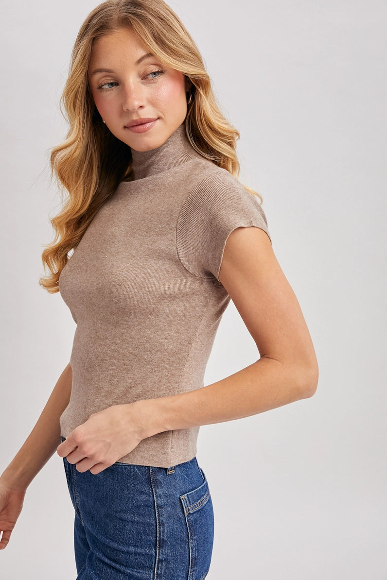 Woman wearing a brown turtleneck top and blue jeans on a white background
