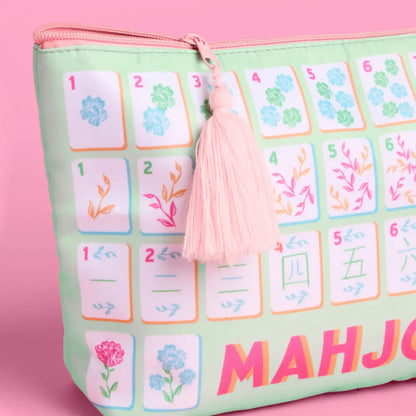 A mint green zippered pouch featuring a printed mahjong tile pattern with a pink tassel zipper pull, set against a solid pink background.
