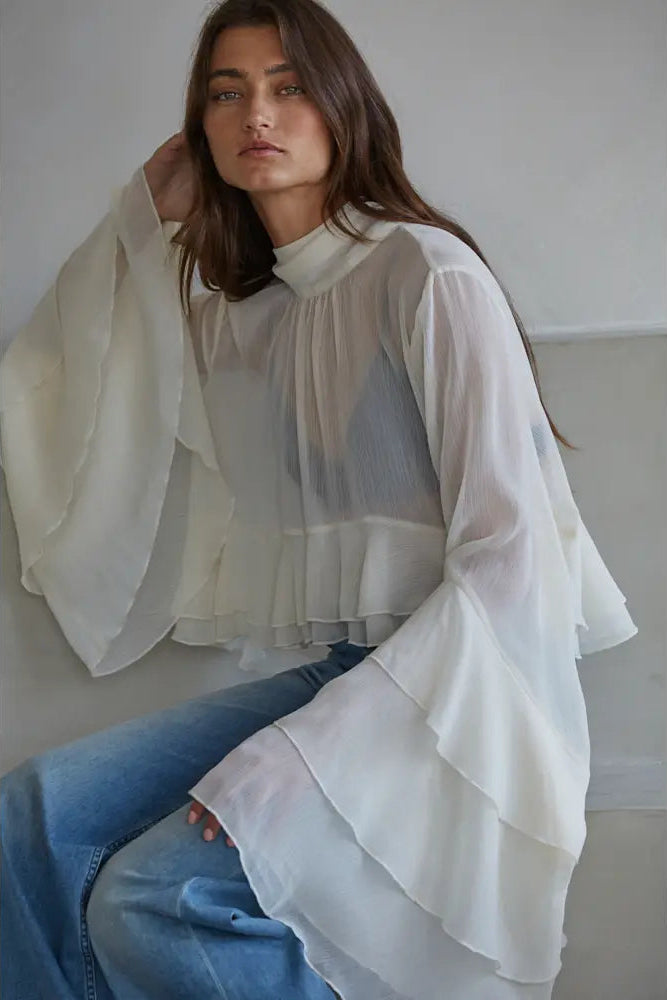 Woman wearing a white layered scarf and blue jeans against a plain background