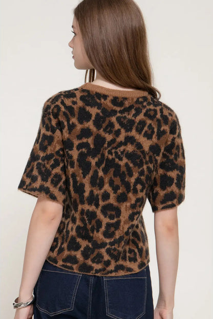 A woman shown from the back wearing a brown and black leopard-print short-sleeve knit top with dark blue jeans, set against a plain light beige background.