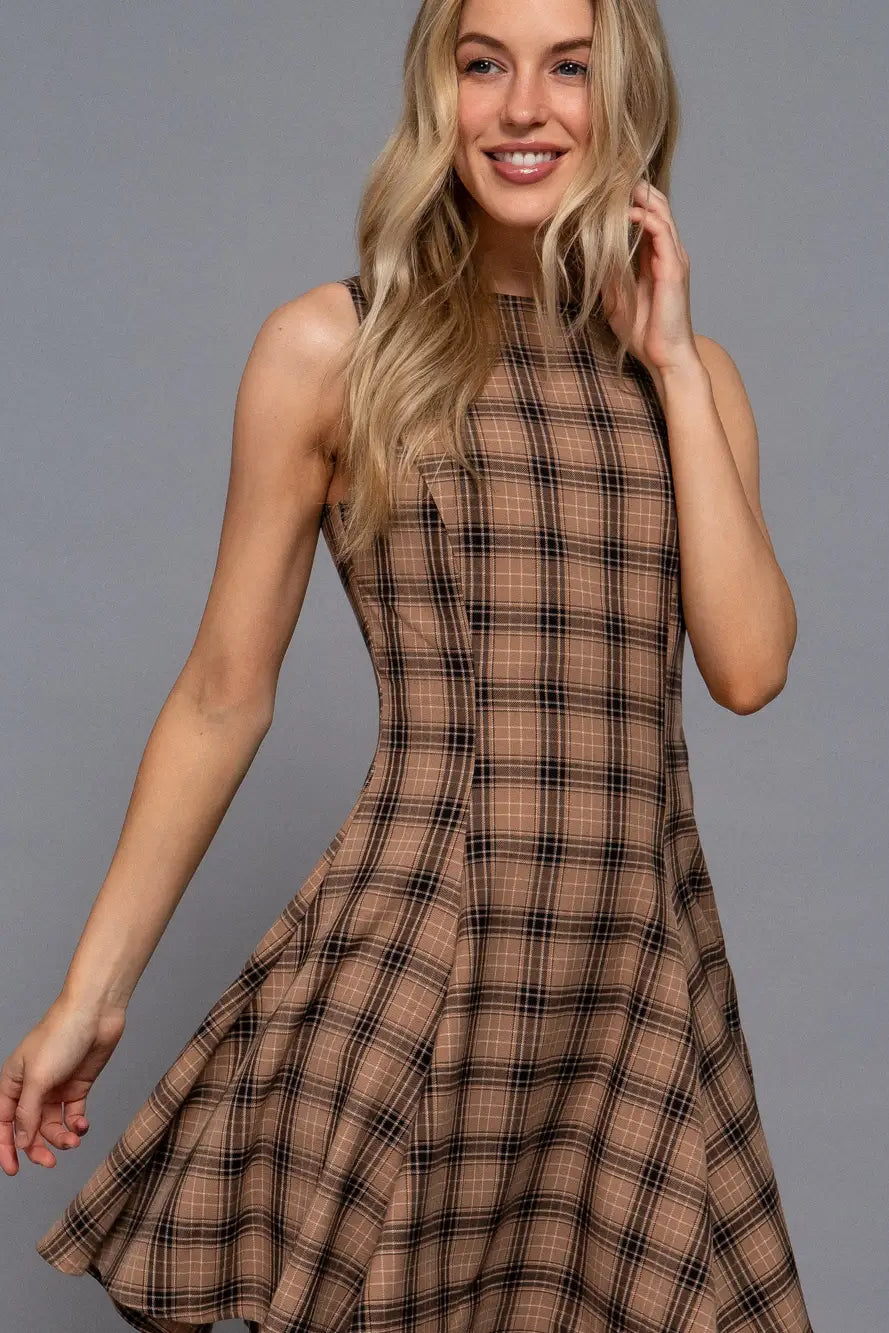 A woman modeling a sleeveless, high-neck, flared A-line dress in a brown and black plaid pattern against a solid gray studio background.