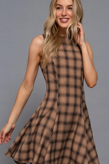 A woman modeling a sleeveless, high-neck, flared A-line dress in a brown and black plaid pattern against a solid gray studio background.