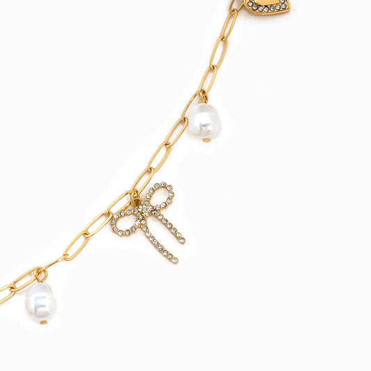 Gold chain necklace with pearl pendants and a bow charm on a white background