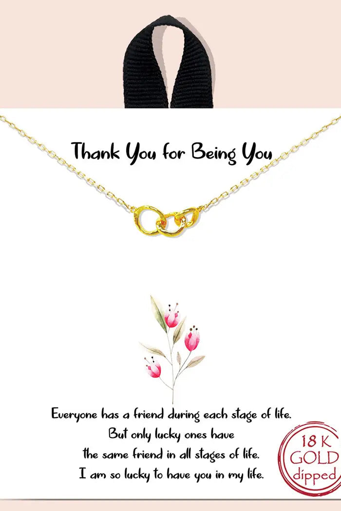 Gold necklace on a card with floral design and text on a pink background