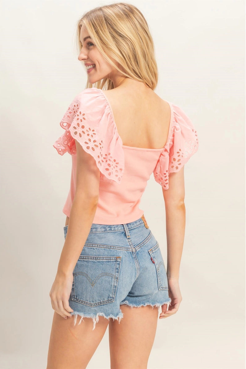 Woman wearing a pink top with lace details and denim shorts on a plain background