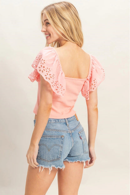 Woman wearing a pink top with lace details and denim shorts on a plain background