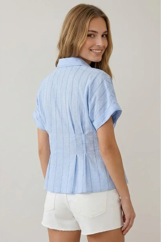 Woman wearing a light blue checkered shirt and white shorts against a plain background
