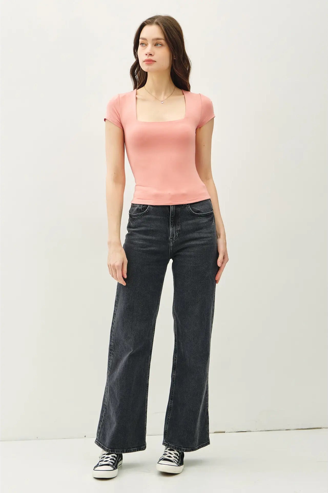 Woman wearing a pink top and black jeans against a white background