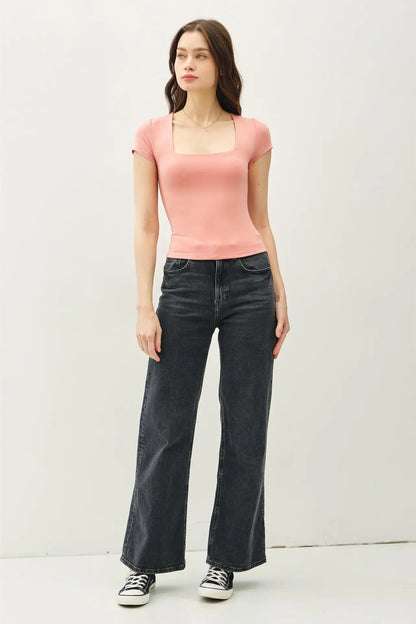 Woman wearing a pink top and black jeans against a white background