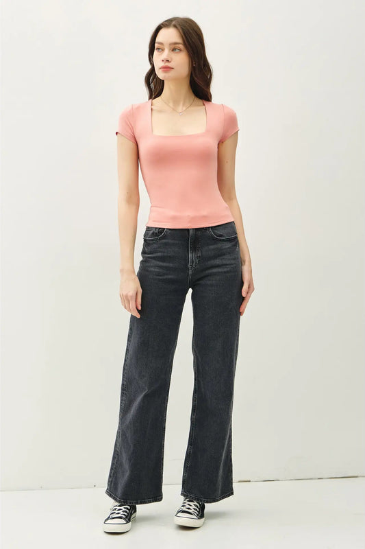 Woman wearing a pink top and black jeans against a white background