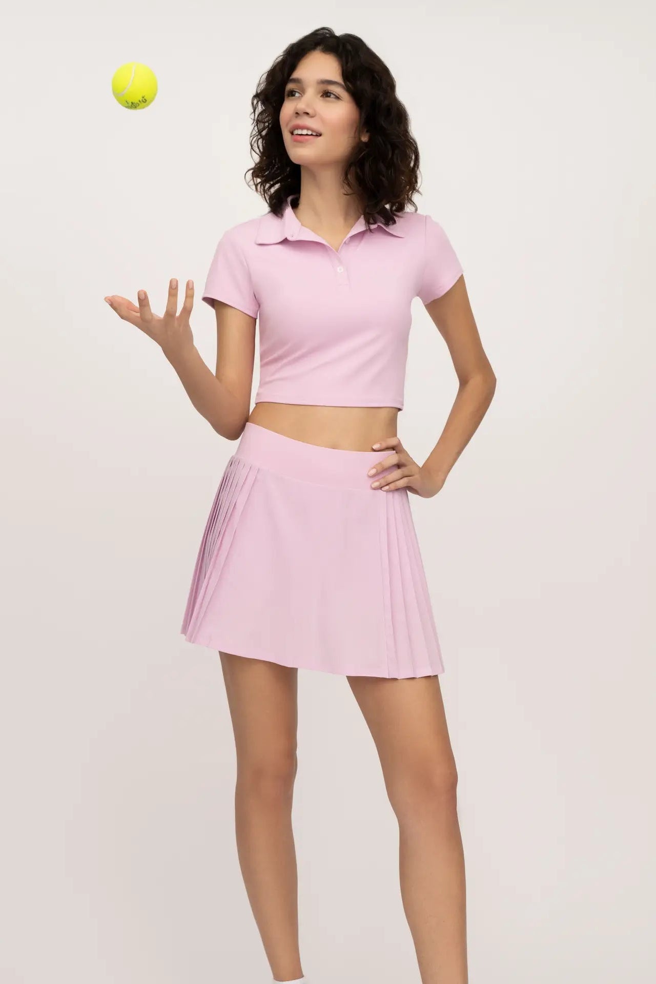 Woman in pink tennis outfit with a tennis ball on a light gray background