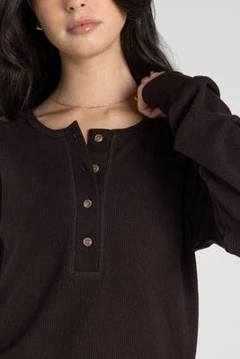 Person wearing a dark brown ribbed sweater with buttons on a light gray background