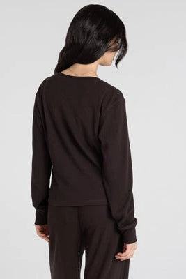 A woman shown from the back wearing a dark brown long-sleeve top and matching dark pants against a light gray studio background.