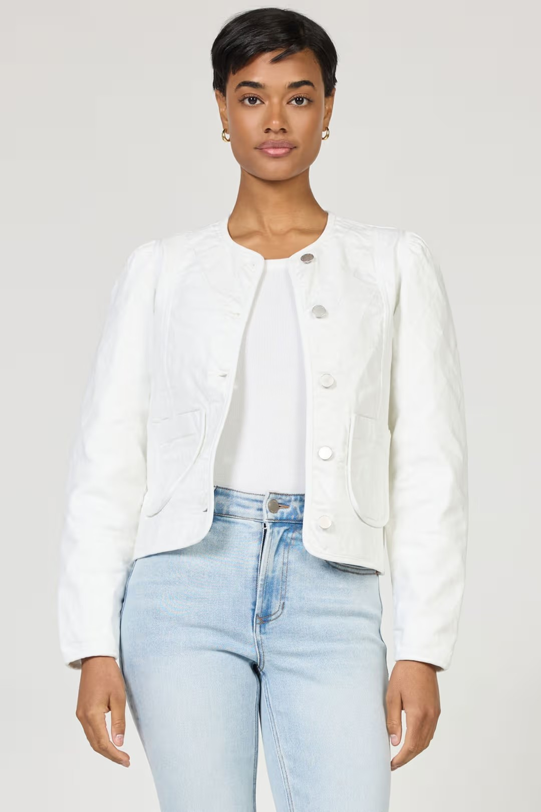 Woman wearing a white jacket and light blue jeans on a plain background