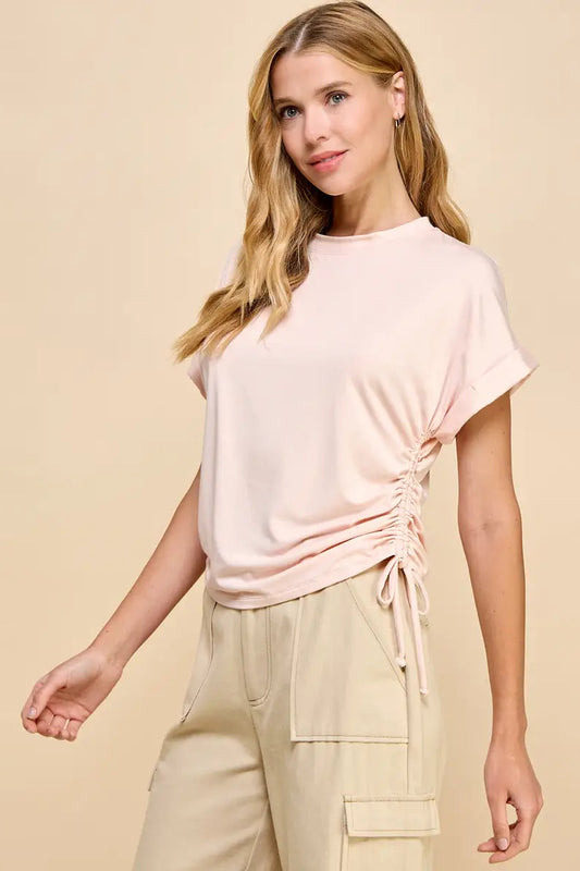 Woman wearing a light pink ruched top and beige pants on a beige background