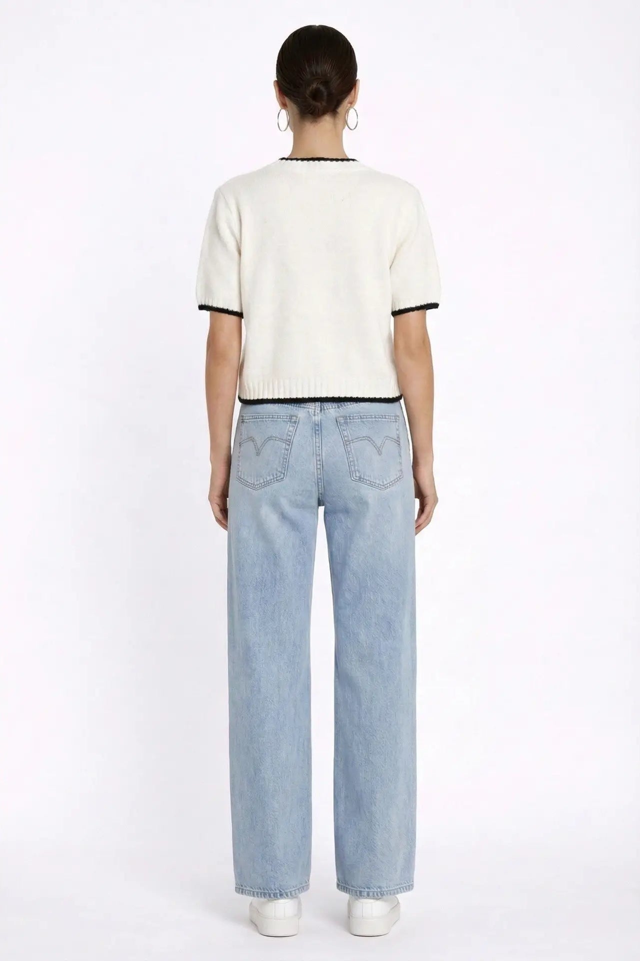 A model shown from the back wearing a cream short-sleeve knit top with black trim and light-wash wide-leg jeans against a plain white studio background.