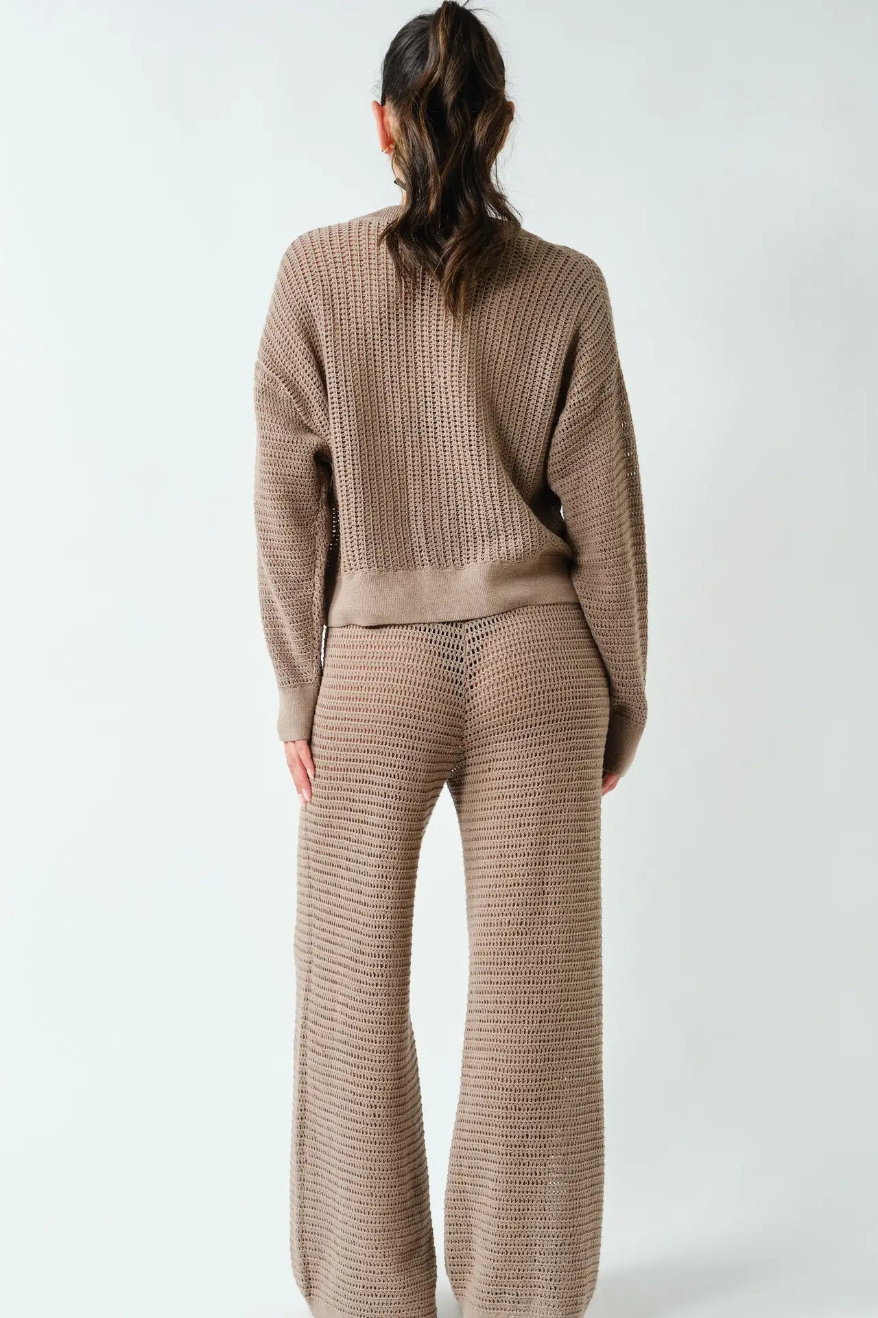 A model viewed from the back wearing a matching knit two-piece set consisting of a long-sleeve sweater and wide-leg trousers in a taupe brown color.