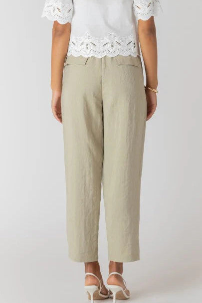 Person wearing a white lace top and beige pants on a plain background