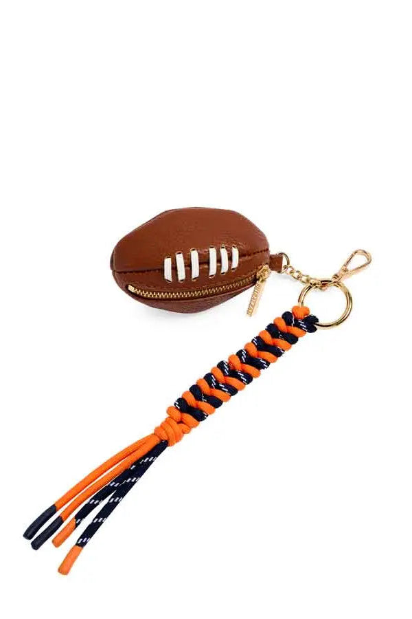 A football-shaped zippered pouch keychain in brown faux leather with white laces, attached to an orange and navy braided cord tassel with gold-tone hardware, shown on a plain white background.