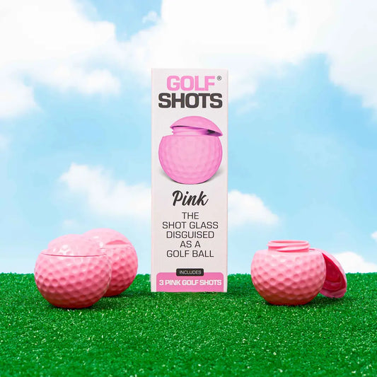 Pink shot glass disguised as a golf ball with packaging on grass against a blue sky.