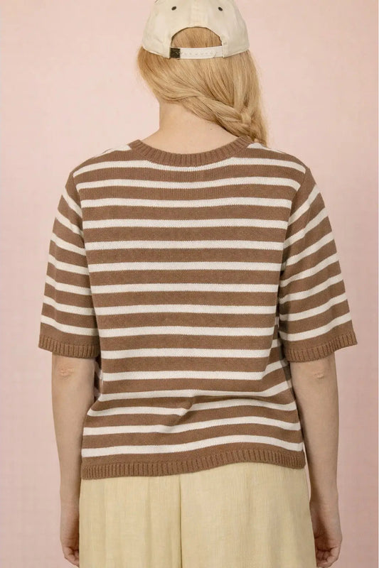 Person wearing a brown and white striped sweater against a pink background
