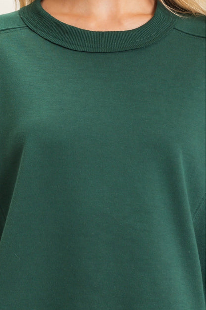 Close-up of a person wearing a dark green crewneck sweatshirt, showing the ribbed collar and smooth fabric texture.