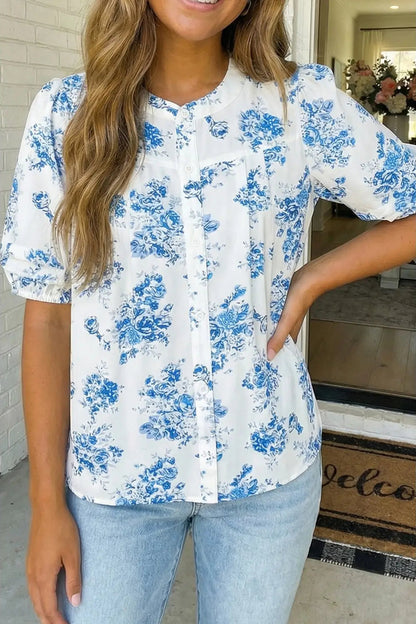 Woman wearing a white blouse with blue floral patterns and light blue jeans indoors.