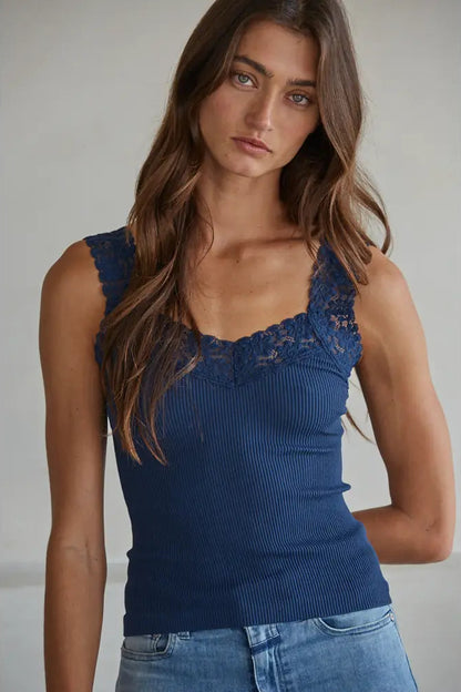 Woman wearing a blue ribbed tank top with lace details against a neutral background
