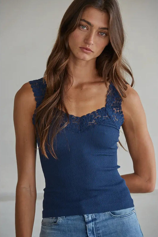 Woman wearing a blue ribbed tank top with lace details against a neutral background