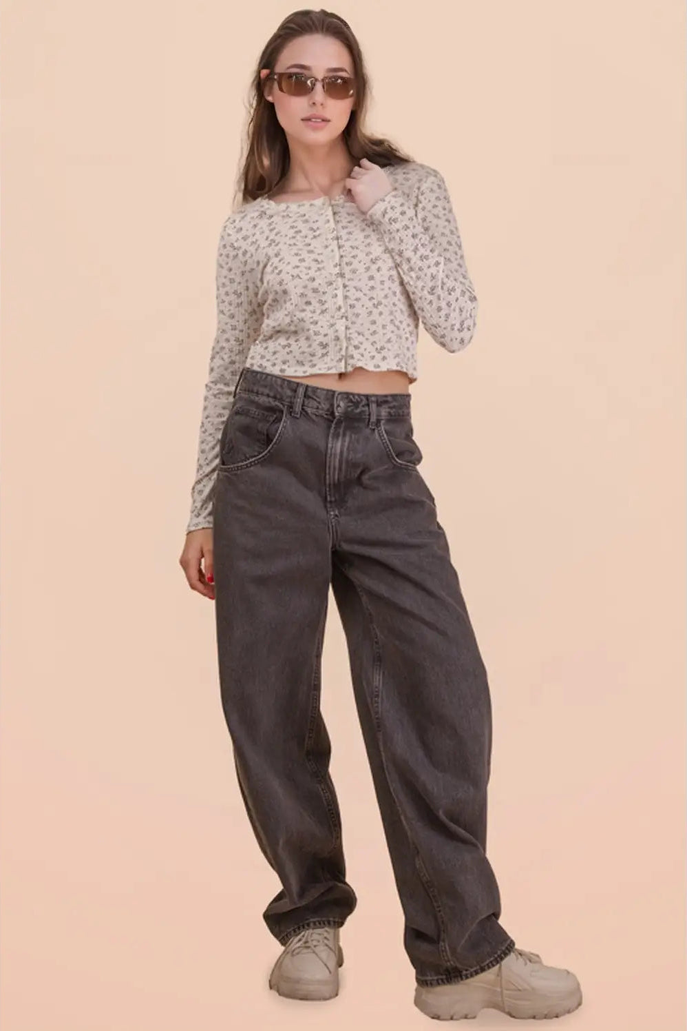 Woman wearing a patterned long-sleeve top and dark jeans against a beige background