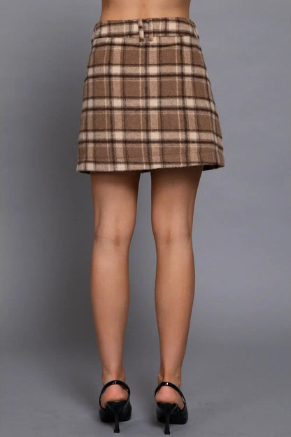 A model's lower body wearing a brown and beige plaid mini skirt with a matching belt, paired with black high heels, against a solid gray studio background.