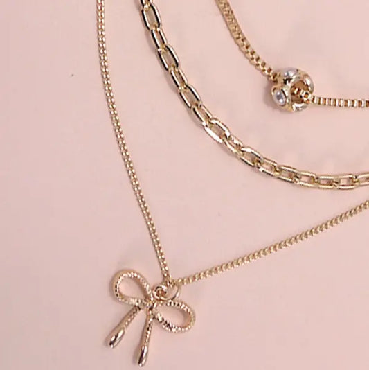 Gold chain necklace with a bow pendant on a pink background