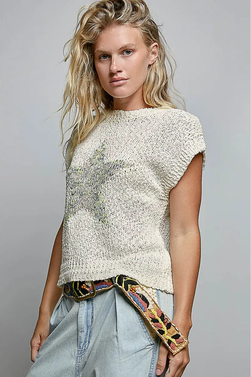Woman wearing a textured white top with a colorful scarf, standing against a gray background