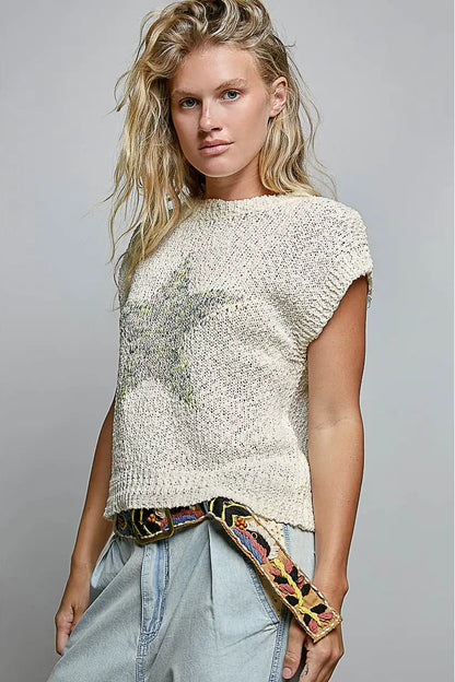 Woman wearing a textured white top with a colorful scarf, standing against a gray background