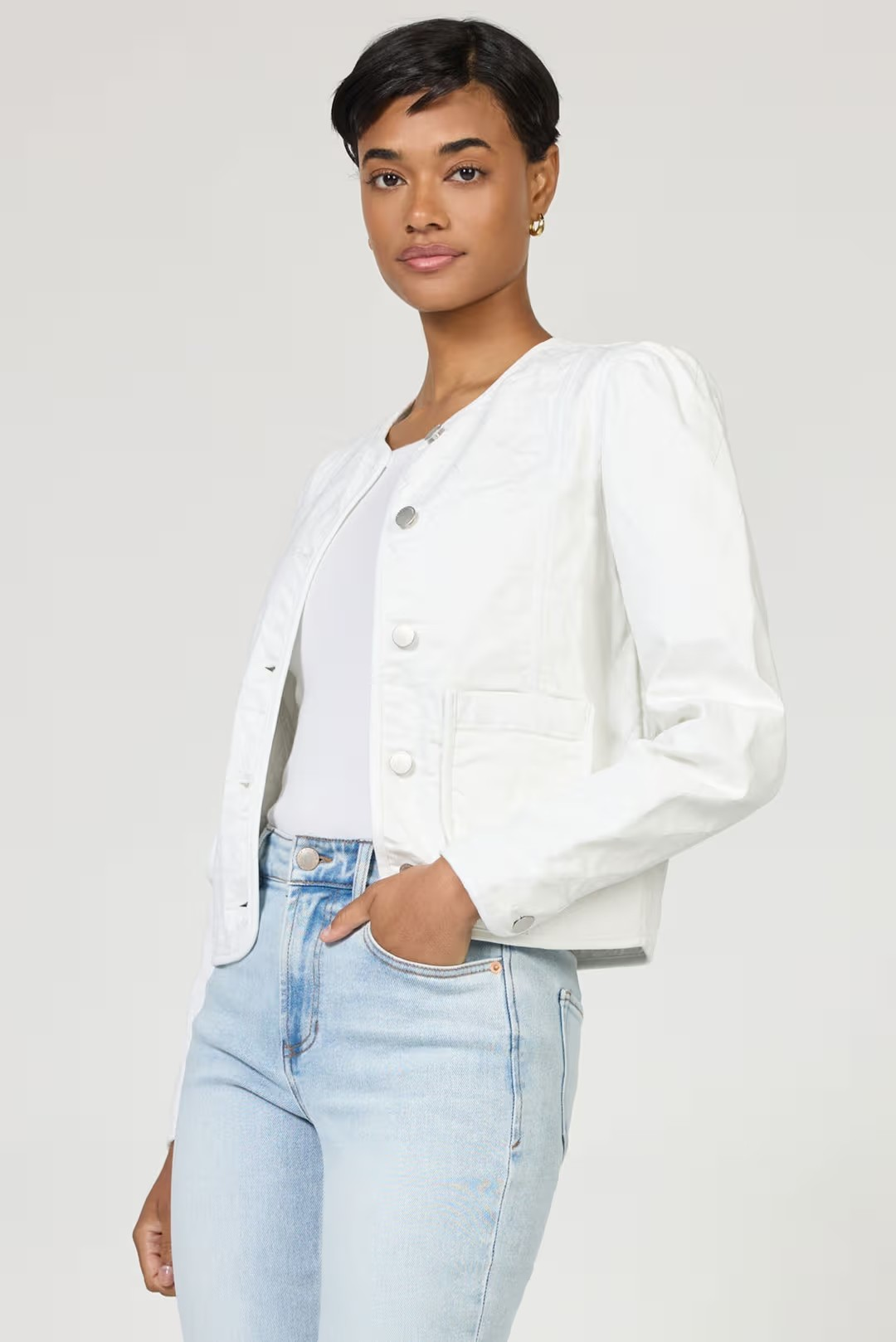 Woman wearing a white denim jacket and light blue jeans on a plain background