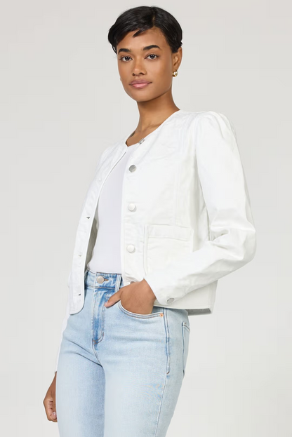 Woman wearing a white denim jacket and light blue jeans on a plain background