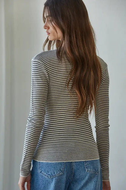 A woman with long brown hair is shown from the back wearing a fitted long-sleeve striped top with blue jeans in a bright indoor setting.