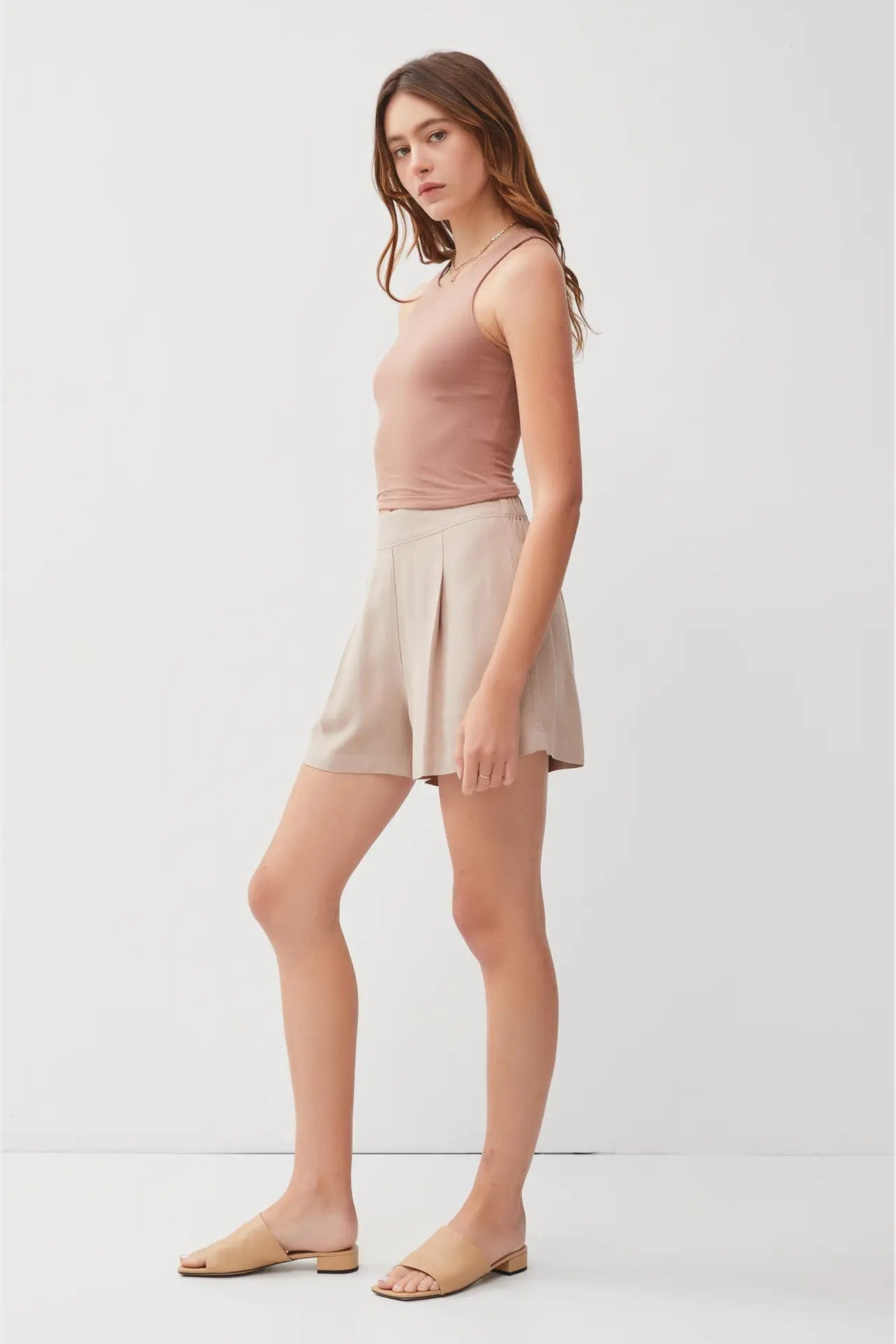 Woman wearing a pink sleeveless top and beige shorts on a white background
