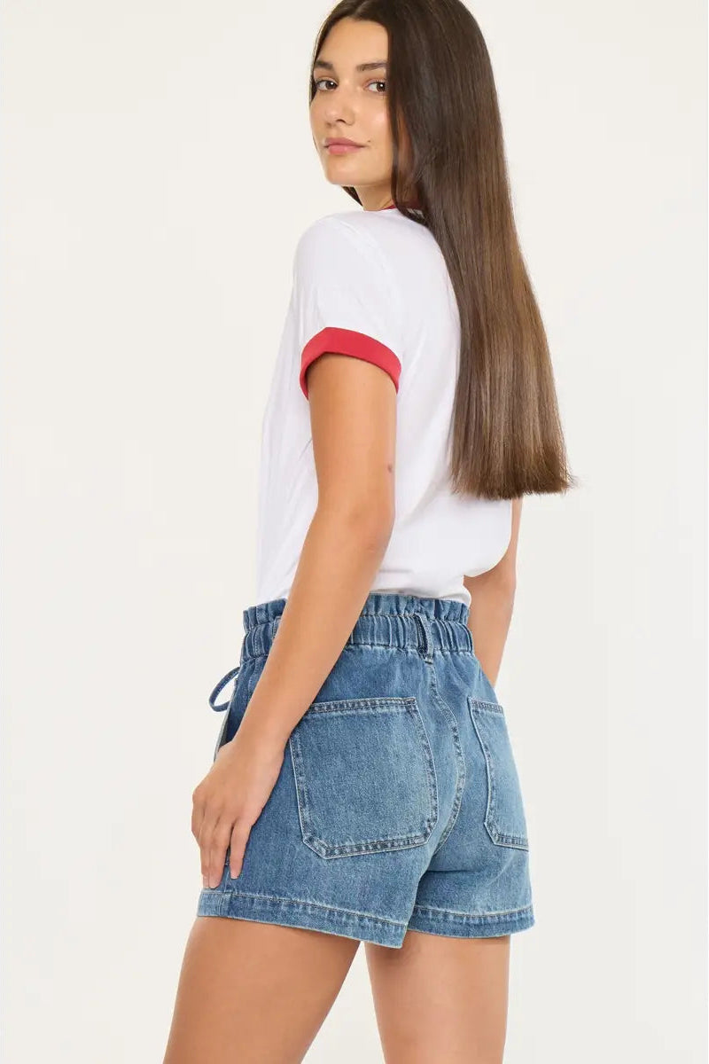 Woman wearing a white t-shirt with red trim and denim shorts on a plain background