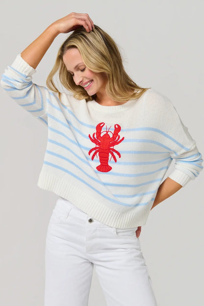 Woman wearing a white sweater with blue stripes and a red lobster design on a plain background