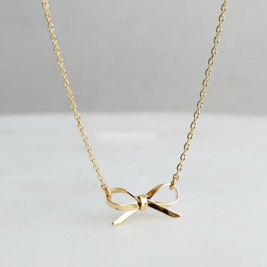 Gold bow-shaped necklace on a light gray background